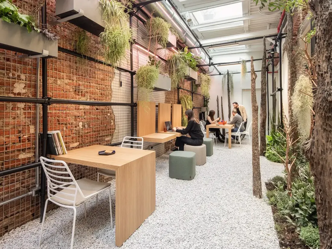 Persone al lavoro tra alberi, piante sospese e arredi del Serendipity Garden